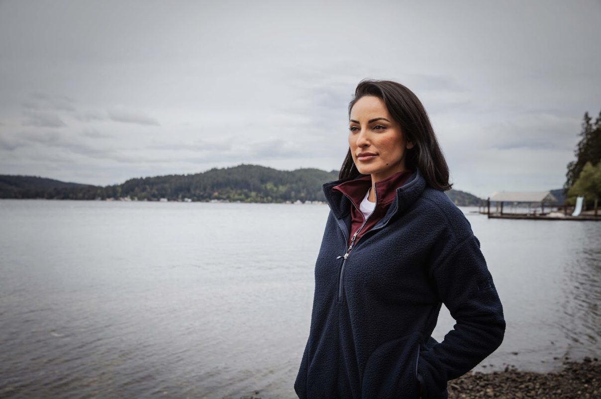 woman standing next to a lake wearing layers